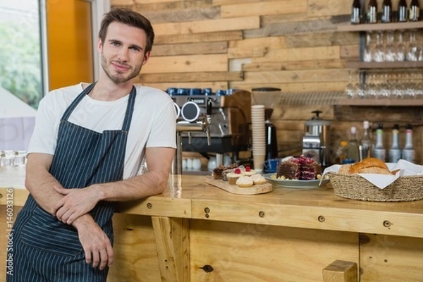 Fototapeta Portrait of smiling waiter leaning at counter