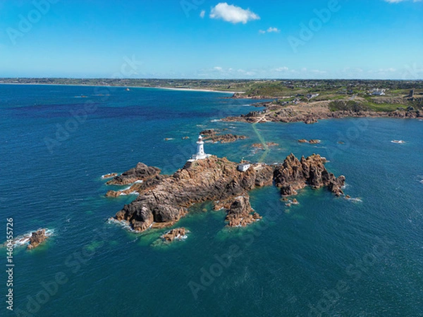 Fototapeta Scenic aerial drone view of La Corbiere lighthouse on a rocky island surrounded by the blue sea. Jersey, Channel Islands