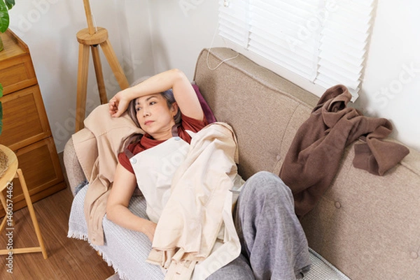 Obraz Exhausted Older Woman Lying on Couch Surrounded by Clothes