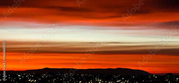 Fototapeta Sunrise in Australia, with city lights in front of a dark mountain range