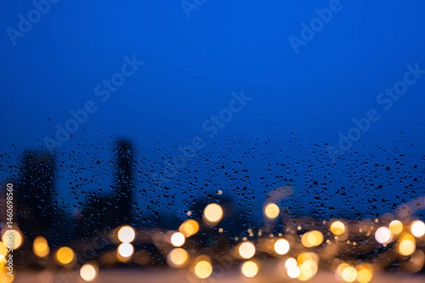 Fototapeta Raindrops on glass window with golden lights and blurred city background.