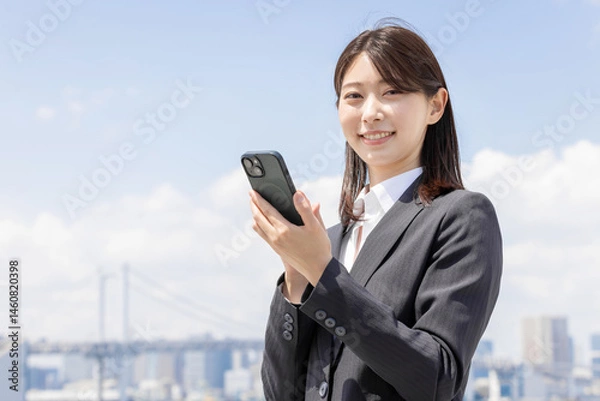 Obraz スマホを持ったスーツの若いビジネスウーマン
