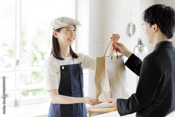 Obraz カウンターで注文品をお客に渡すカフェの女性店員
