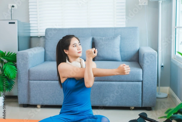 Obraz Young Asian woman practices yoga by stretching her back on a yoga mat in the living room at home. She performs pilates with challenge and motivation for health, fitness, and wellbeing