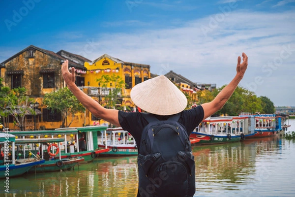 Fototapeta back of happy male tourist traveler in a Vietnamese hat on a bridge in old town in Hoi An in Vietnam in Asia