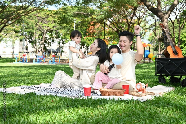 Obraz A family of four is sitting on a blanket in a park, enjoying a picnic together.