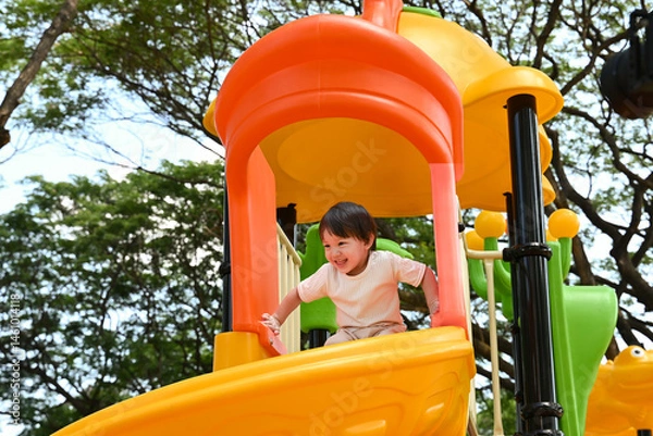 Obraz A young child is playing on a yellow and orange play structure. The child is smiling and he is enjoying the activity.