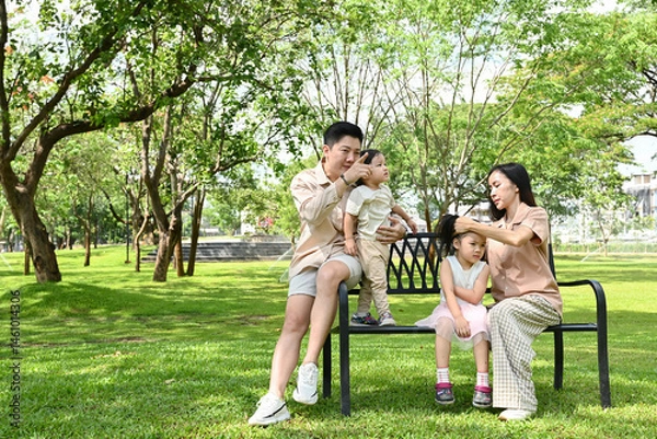 Obraz A family of four sits on a park bench, enjoying each other's company.