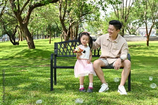 Obraz A man and a little girl are sitting on a park bench, Scene is warm and friendly, as the man and the girl seem to be enjoying each other's company.