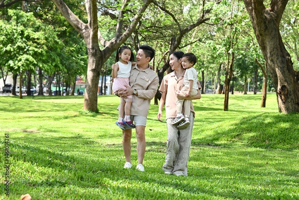 Obraz A family of four is walking in a park, the family appears to be happy and enjoying their time together.