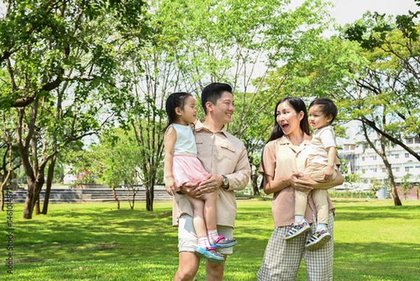 Obraz A family of four is walking in a park, the family appears to be happy and enjoying their time together.