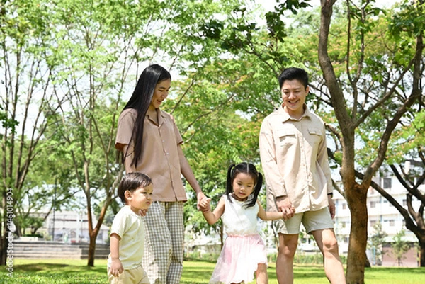 Obraz A family of four is walking in a park, the family appears to be happy and enjoying their time together.