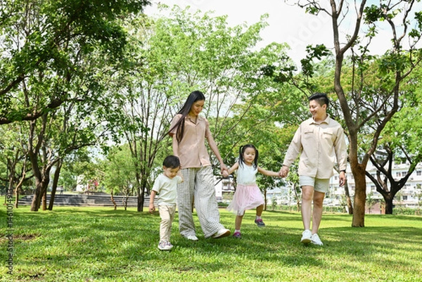 Obraz A family of four is walking in a park, the family appears to be happy and enjoying their time together.
