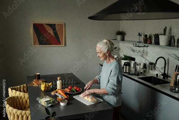 Fototapeta Elderly woman preparing meal with fresh vegetables and ingredients in modern kitchen setting with various kitchen tools around countertop
