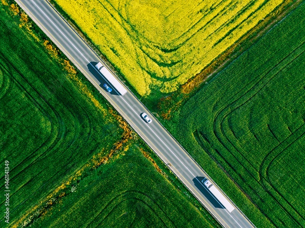 Fototapeta Aerial view of white trucks and cars driving on asphalt road along the green and yellow fields in Finland. Cargo delivery logistic concept