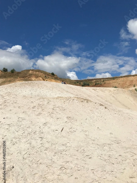 Fototapeta A wide shot of a sandy hill with a bright blue sky and white clouds above. Ideal for travel, outdoor activities, and nature-themed projects.