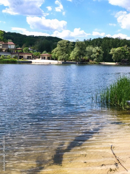 Fototapeta A serene landscape of a river with clear water, surrounded by lush greenery and a sandy shore. TIdeal for relaxation, travel, and outdoor-themed projects.