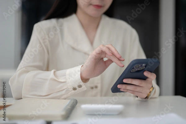Fototapeta Close up of a female office worker hand hovering over phone while sitting at working table in office