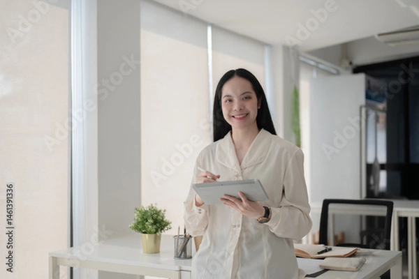 Fototapeta Female office worker is holding a stylus writing on tablet while standing in front of working table.
