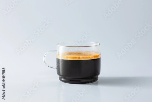 Fototapeta A clear glass cup filled with freshly brewed espresso, showcasing rich crema on top. Minimalist composition on a clean white background, perfect for coffee or lifestyle concepts.