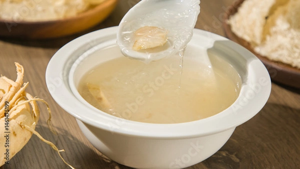 Fototapeta Close-up of a spoon scooping bird's nest strands out of a porcelain bowl. The bowl of the bird's nest is opaque white in color and has a thick texture. Bird's nest is a nutritious source of protein.