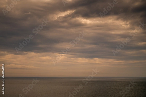 Fototapeta Sun between dark storm clouds over ocean. Dramatic seascape. Clouds and rain flurry over sea.