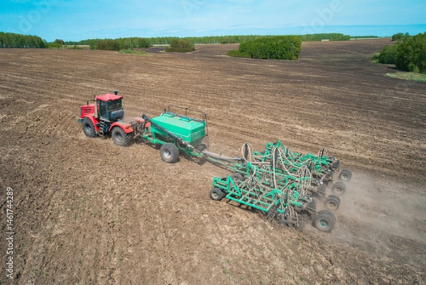 Fototapeta A red tractor is actively tilling a large, flat agricultural field