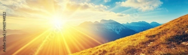 Obraz Golden sunset over mountain peaks.  Sunlight rays stream down a hillside covered in tall grass