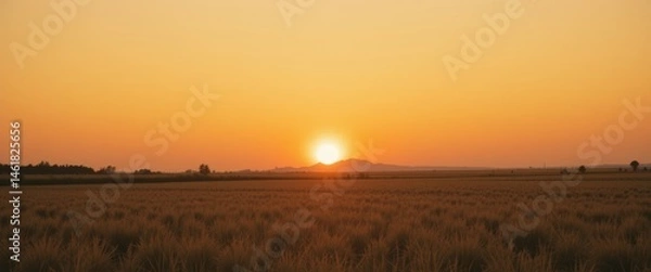 Fototapeta A stunning sunset over a flat landscape with a vibrant orange sky and the sun dipping below the horizon, perfect for travel, landscape, or nature background themes.