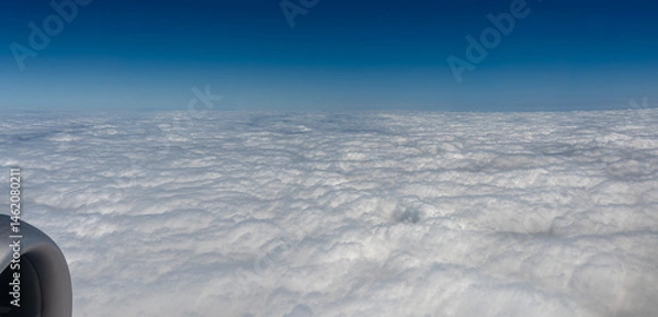 Fototapeta View from a plane window looking down on thick clouds with a blue color cast
