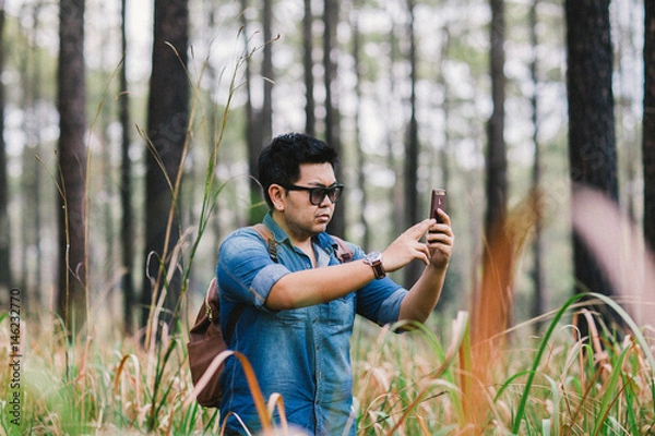 Fototapeta A man with his mobile smart phone searching for reception signal in the forest.