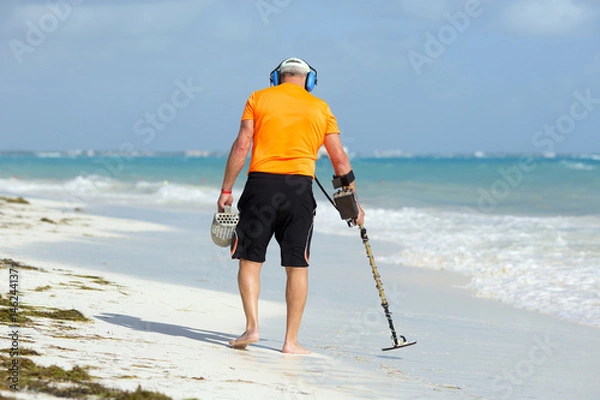 Fototapeta A man is walking on the beach with metal detector to find jewellery and coins.