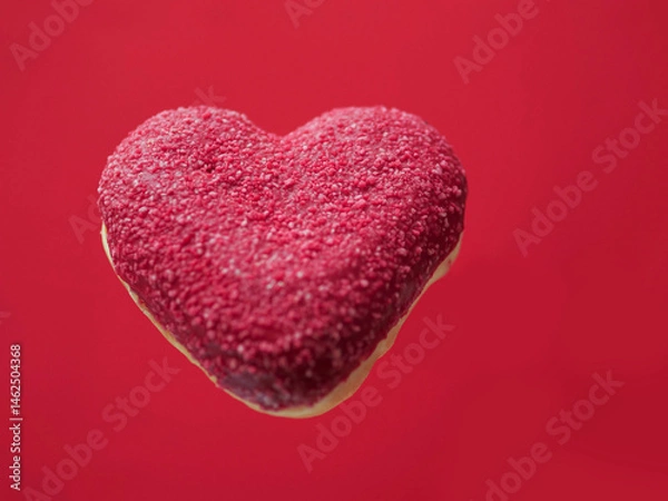 Fototapeta Red creative heart shaped donut floating in the air, red color saturated background. Love and romance concept. Valentine gift idea. Transforming food for marketing reasons to increase sales.