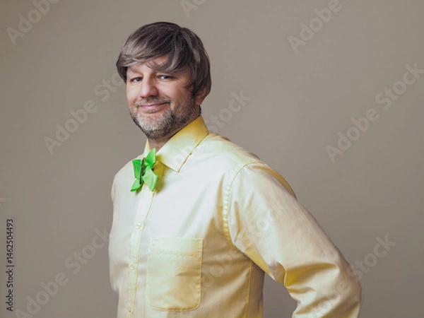 Fototapeta Man in yellow shirt and green bow with shamrock on light color background. Irish sport supporter or fan. Model in his 40s or 50s with grey beard and hair.