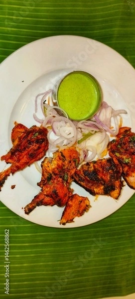 Fototapeta a plate of Tandoori Chicken, a popular Indian dish. The chicken pieces are marinated in a mixture of yogurt and spices, giving them a deep red or orange color, and then cooked in a tandoor 