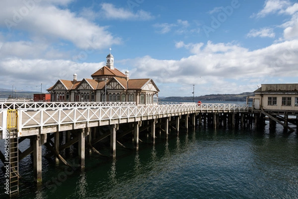 Fototapeta Victorian Dunoon timber ferry pier in Scotland, Category A listed wooden structure in Firth of Clyde closed to public needs renovation. Pretty historic landmark buildings on greenheart timber piles 