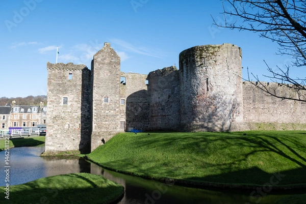 Fototapeta Rothesay Castle ruin and moat on the Scottish island of Bute with stone circular plan towers and curtain walls on sunny summer blue sky day