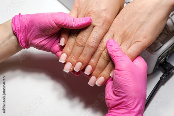 Obraz French Manicure Finish at Beauty Salon, Close-up of freshly done French manicure with pink and white tips, held by gloved hands.
