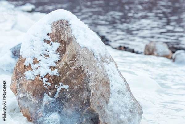Fototapeta A large rock covered in snow sits on a frozen lake