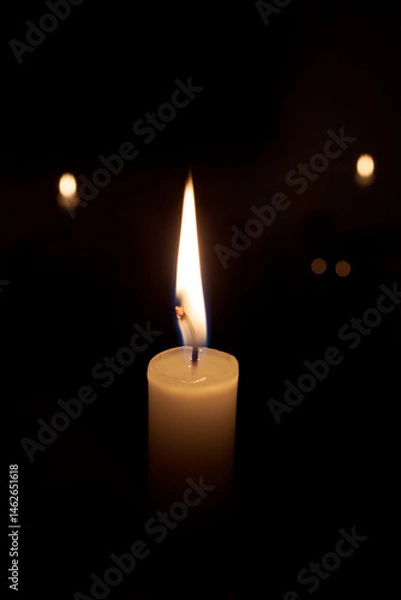 Fototapeta the flame from a candle on a black background, the lights are blurred from behind