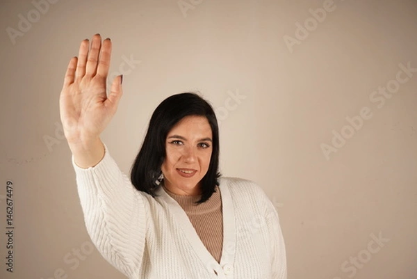 Fototapeta The friendly gesture signals a joyful "hello" or a casual goodbye. Her casual demeanor creates a welcoming atmosphere. A smiling girl waves her hand in a cheerful greeting, radiating warmth.