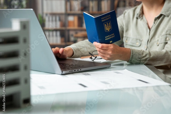 Fototapeta Close up female hands  with Ukraine passport entering data using laptop .
