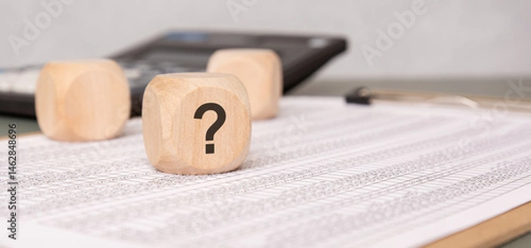 Obraz Wooden block with question mark on financial document, symbolizing uncertainty