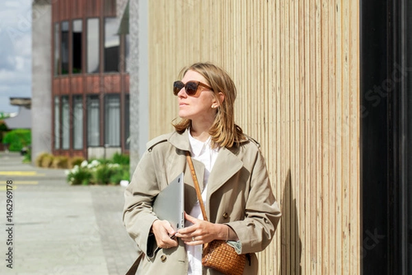 Obraz Confident woman outdoors wearing stylish coat with laptop and sunglasses. Businesswoman 