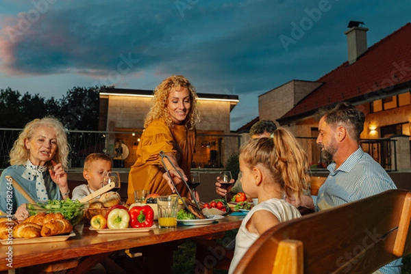Fototapeta Family enjoying barbecue dinner on patio in the evening