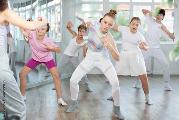 Fototapeta Female girl student repeats movements of unrecognizable teacher during group modern dance class. Hobbies, active pastime, additional extracurricular activities for children and teenagers