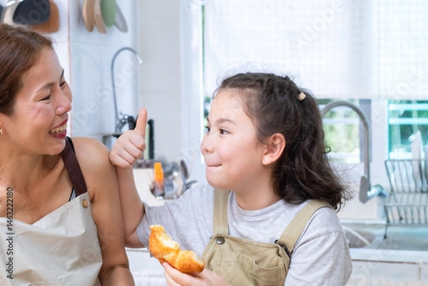 Fototapeta Smiling mother pouring orange juice into a glass for cheerful daughter, capturing family bonding and care, woman and child sharing a happy moment, happiness and warmth in kitchen atmosphere