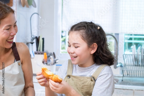 Fototapeta Smiling mother pouring orange juice into a glass for cheerful daughter, capturing family bonding and care, woman and child sharing a happy moment, happiness and warmth in kitchen atmosphere