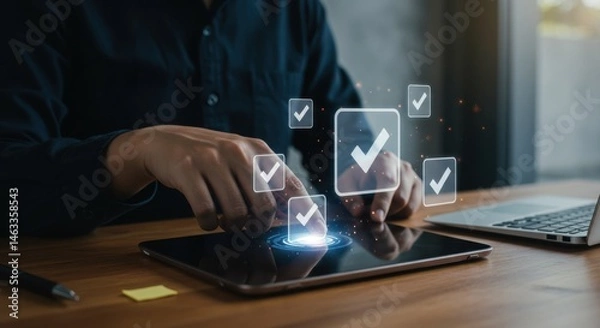 Fototapeta Person using tablet with check mark icons and laptop on desk in office space