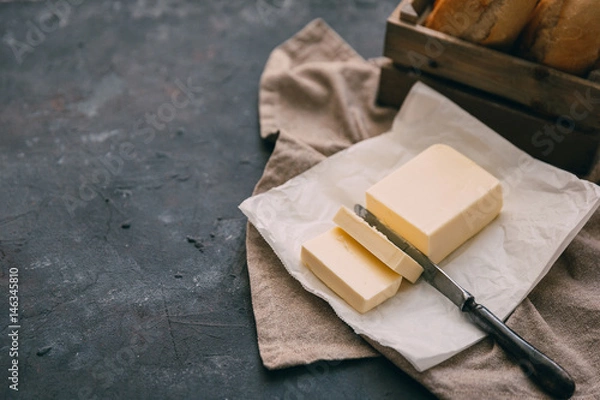 Obraz Pat of fresh farm butter  with a knife and bread over rustic background